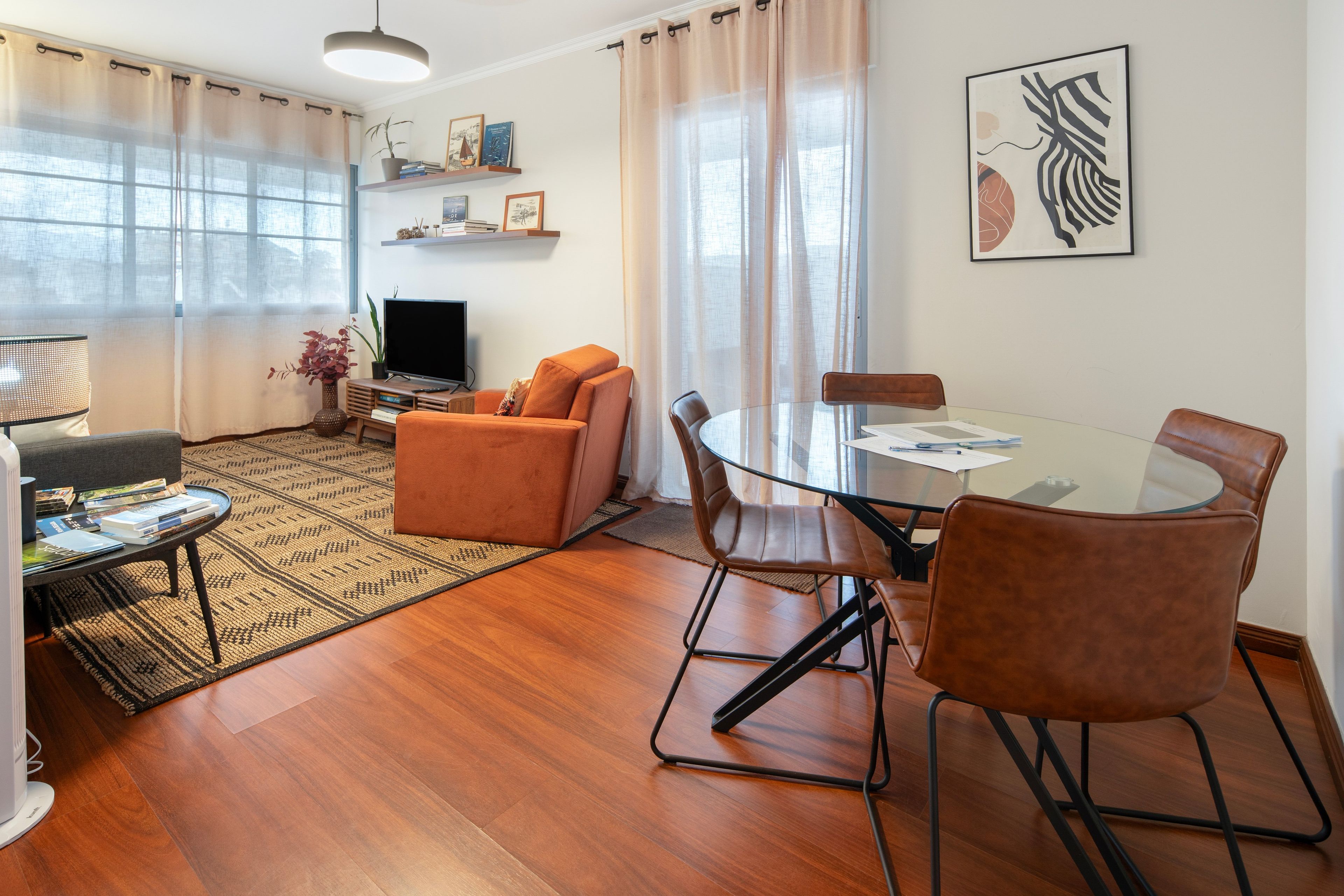 A modern living room with a sofa, a glass dining table with chairs, a TV, and a bookshelf with decorative items.