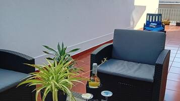 Terraço no telhado com mobiliário de exterior, um vaso de planta, uma garrafa de vinho e um livro.