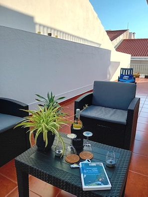 Terraço no telhado com mobiliário de exterior, um vaso de planta, uma garrafa de vinho e um livro.