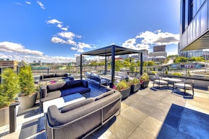 Eine Dachterrasse mit Sitzgelegenheiten im Freien, Topfpflanzen und Blick auf die Stadtlandschaft.