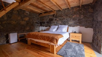 Un dormitorio con pared de piedra, vigas de madera en el techo, cama, mesitas de noche y un calentador.