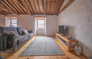 A cozy living room with a sofa, a TV, a wooden table with books, and a window.