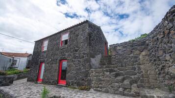 Ein Steinhaus mit zwei roten Türen und einem kleinen Fenster, umgeben von einer Steinmauer und einem Kopfsteinpflasterweg.
