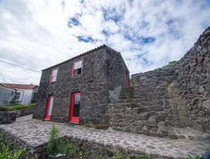 Un edificio de piedra con dos puertas rojas y una ventana pequeña, rodeado de un muro de piedra y un camino adoquinado.