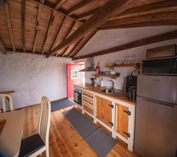 Cocina compacta con vigas de madera, horno empotrado, microondas y refrigerador.