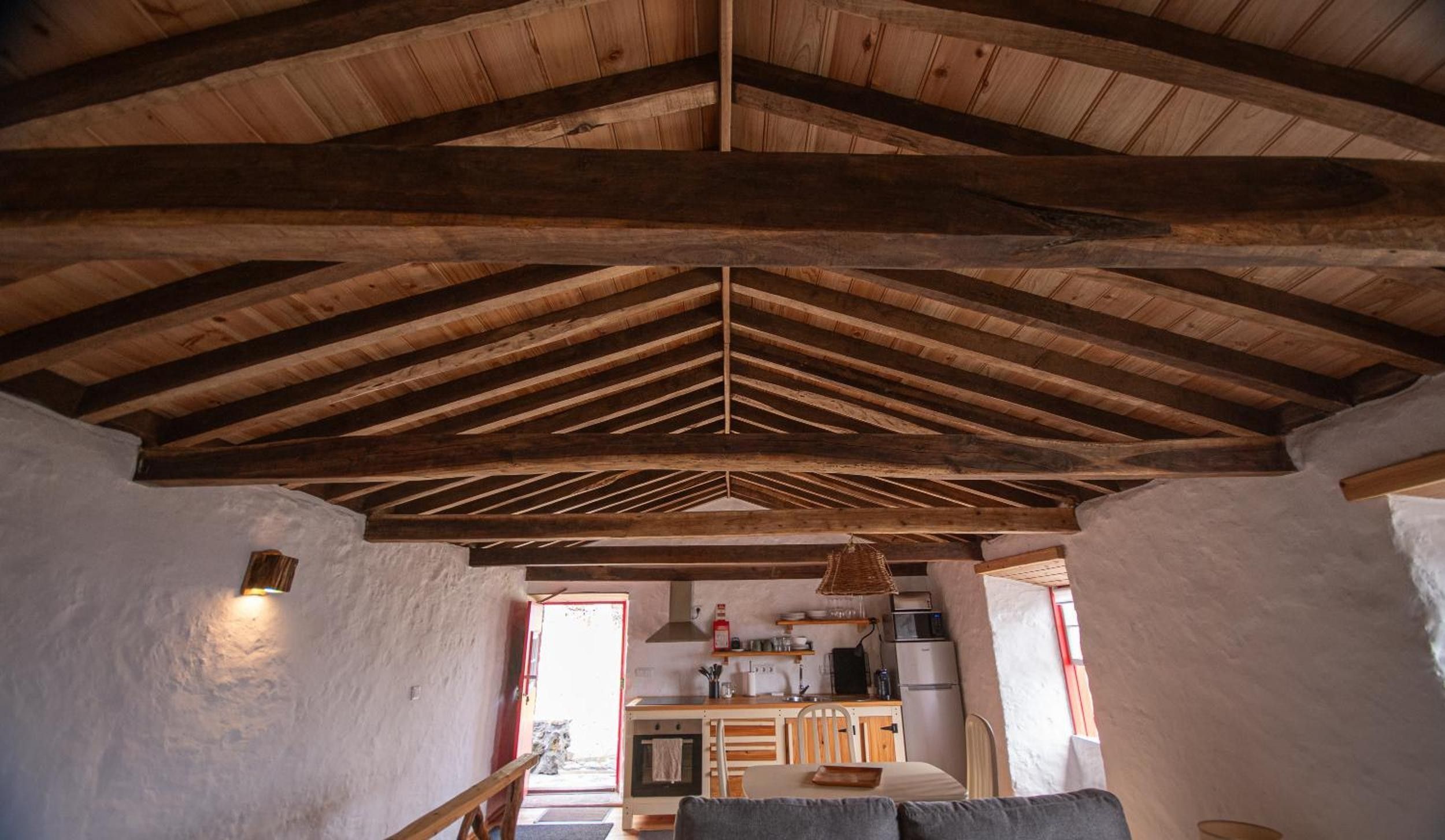 Un interior rústico con un alto techo de madera, una zona de cocina con electrodomésticos básicos y un área de estar con sofá.