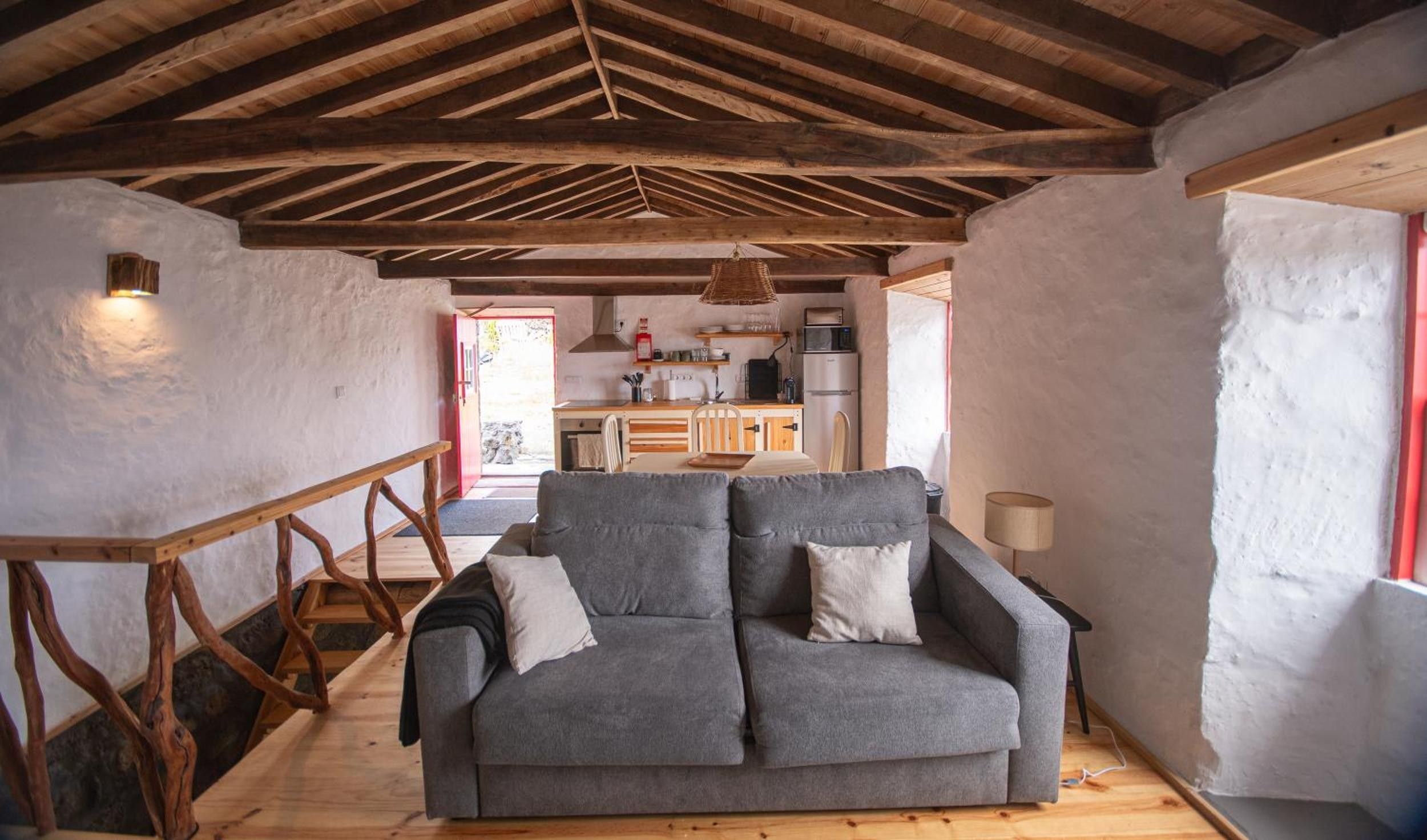 A cozy living room with a sofa, wooden beams, and a kitchen in the background.