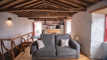A cozy living room with a sofa, wooden beams, and a kitchen in the background.