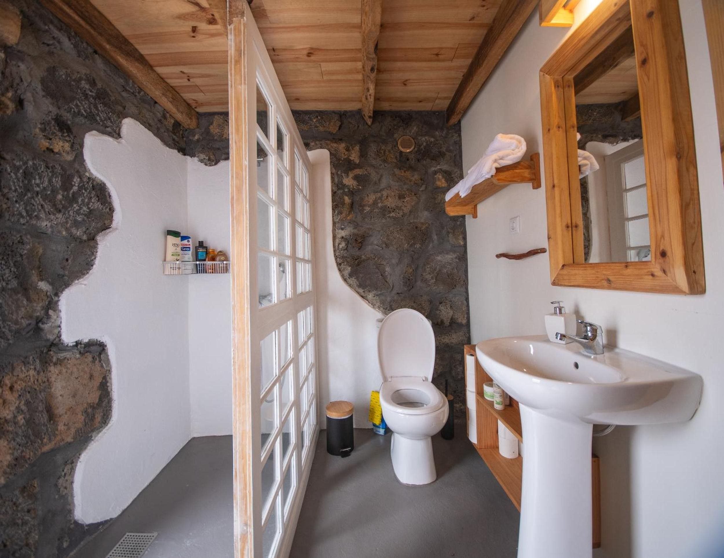 Et badeværelse med stenvæg, træloft, hvid toilet, vask og spejl.