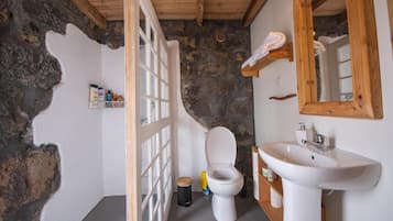 Et badeværelse med stenvæg, træloft, hvid toilet, vask og spejl.