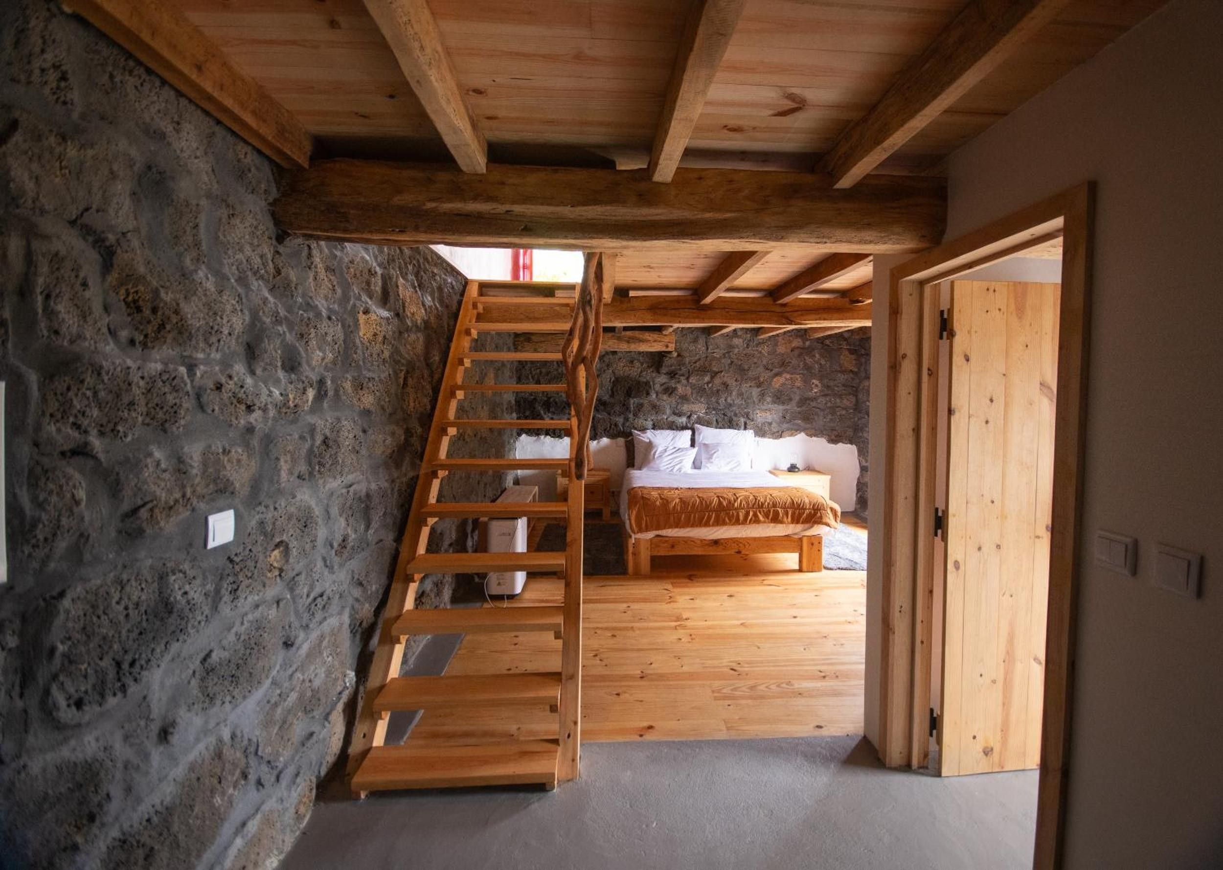 Una camera da letto con un letto di legno, un muro in pietra e una scala in legno.