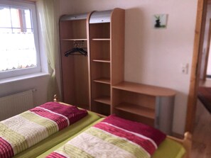 Ett sovrum med ett fönster, en säng med ett randigt överkast, en trägarderob och en liten växt på väggen.