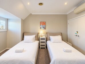 A hotel room with two beds, a nightstand, a lamp, a wall-mounted air conditioner, and a window with blinds. - Camberwell 3BR, 3 Bathrooms | Courtyard & Parking (Camberwell)