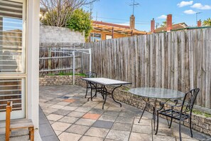 A patio area with a table and chairs, a wooden fence, and a brick wall. - Camberwell 3BR, 3 Bathrooms | Courtyard & Parking (Camberwell)