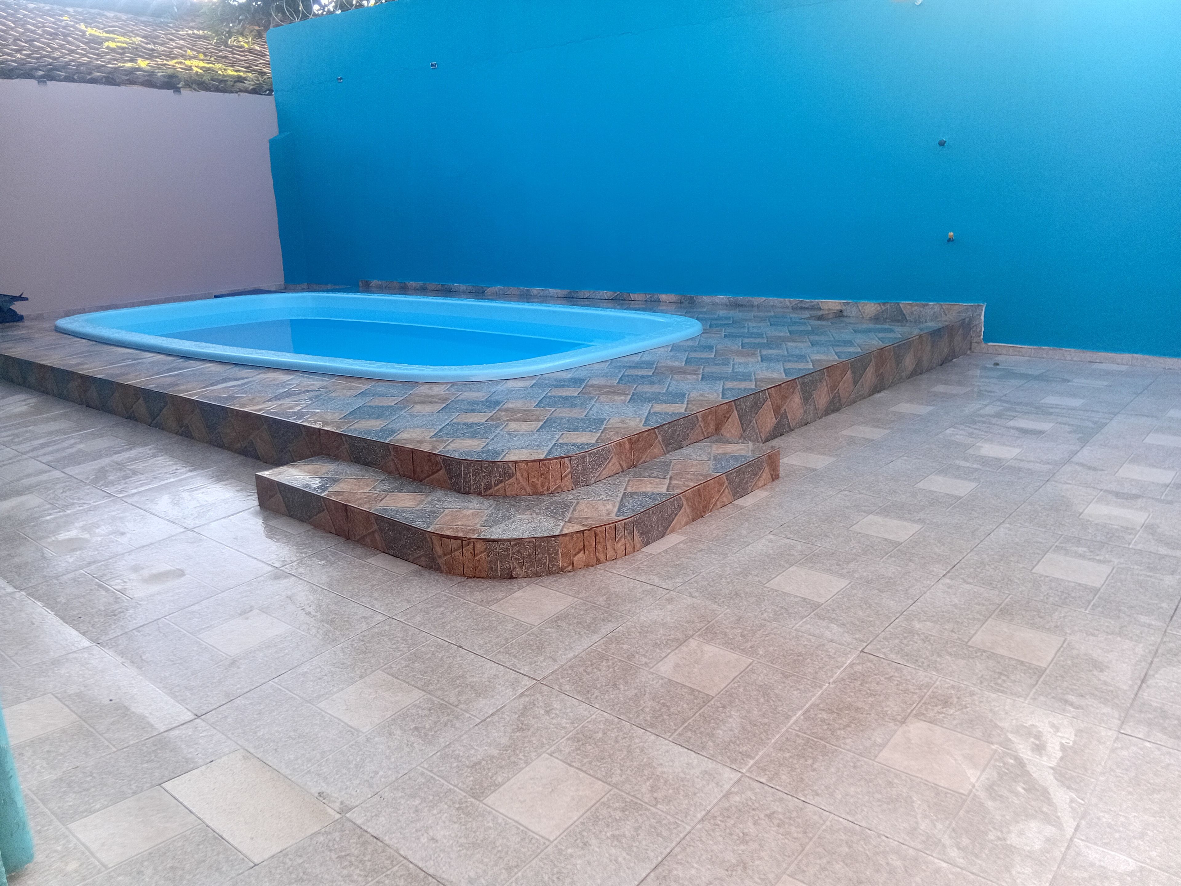 Una piscina con interior azul, rodeada por una solana de piedra con un diseño en espiga.