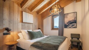 A wooden-paneled bedroom with a bed, bedside table, and a hanging light fixture. - Altamira – Views| Terrace| Hammam| Alpe d’Huez (Huez)