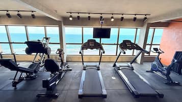 Academia com esteiras, remo e bicicleta ergométrica, com vista para um corpo de água.