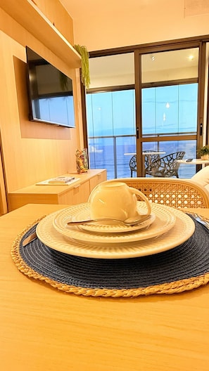 Un comedor con una mesa preparada para dos personas, un televisor montado en la pared y vistas al mar a través de amplios ventanales.
