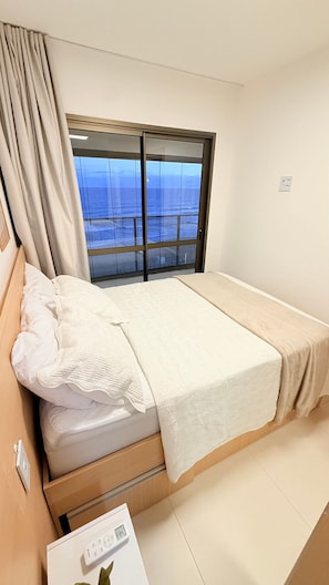 A single bed with a view of the sea through a large window.