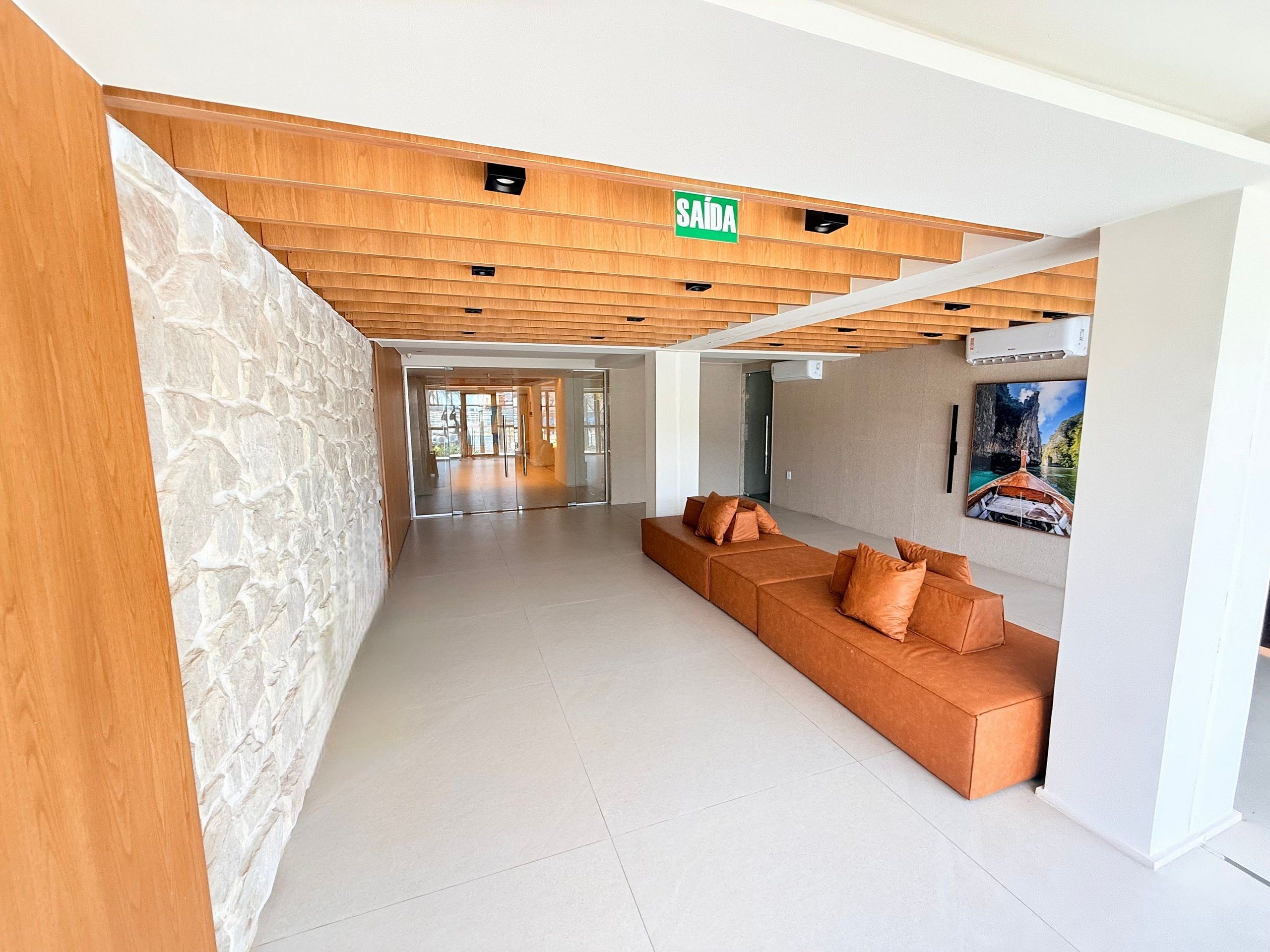Un vestíbulo moderno con techo de madera, pared de piedra, zona de estar con cojines y un cuadro enmarcado.
