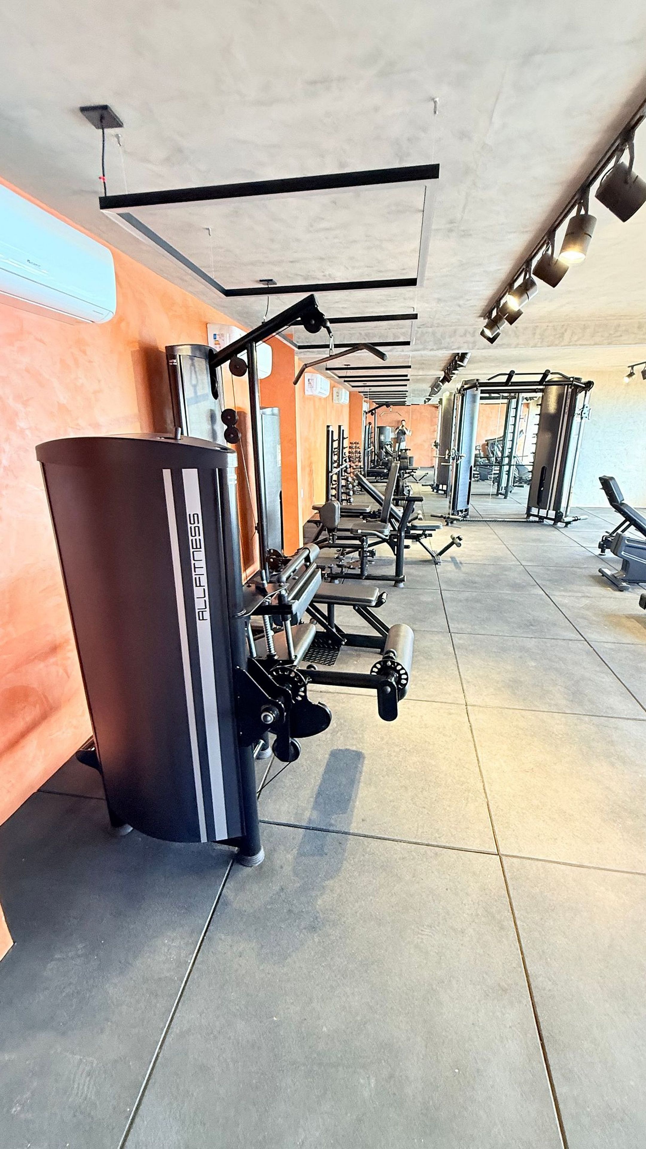 Un gimnasio con diversos equipos de ejercicio, incluyendo cintas de correr y máquinas de pesas, dispuestos en filas.