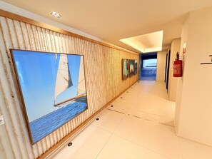 A hallway with a large sailboat painting on the left, a fire extinguisher on the right, and a ceiling light.