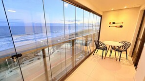 Un balcón con vista a la playa y al océano. Hay una mesa con sillas y un adorno en la pared.