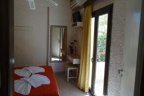 A hotel room with a bed, a desk, a mirror, a television, and a sliding door to the outside. - Holiday Home in Paleochora With Parking (Kantanos-Selino)