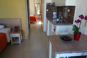 A compact hotel room with a kitchenette, a bed with an orange bedspread, a small bedside table, and a potted plant on the table. - Holiday Home in Paleochora With Parking (Kantanos-Selino)