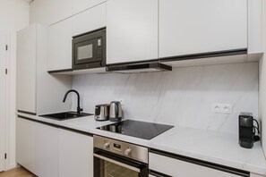 Une cuisine moderne avec des meubles blancs, un four à micro-ondes encastré, un évier en acier inoxydable, une bouilloire et une machine à café.