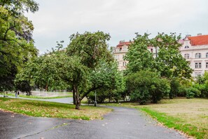 A park with a paved path, trees, and a building with a red roof in the background. - Blueground residence Prague 2  (Prague)