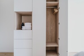 A minimalist closet with wooden doors, a hanging rod, and neatly folded towels. - Blueground residence Prague 2  (Prague)