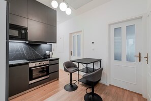 Kompakti keittiö, jossa on modernit kodinkoneet, ruokapöytä ja tuoli.