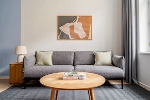 A modern living room with a grey sofa, a round wooden coffee table, and a framed abstract painting on the wall. - Blueground residence Prague 2  (Prague)