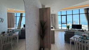 A modern living room with a dining area, large windows with a view of the sea, and a flat-screen TV. - Lovely Sea View Studio in Downtown F285O (Seef)