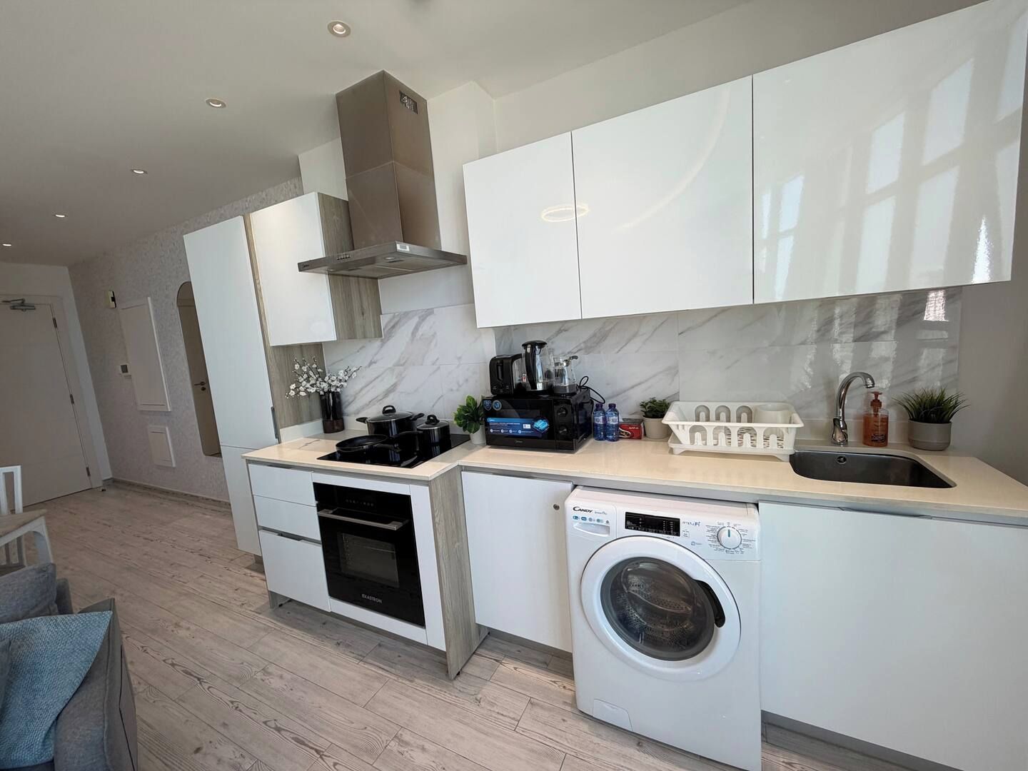 A modern kitchen with a built-in oven, microwave, and dishwasher, a compact washer, and a compact sink.