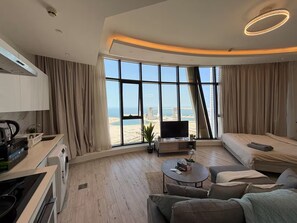 Et moderne hotelværelse med et stort vindue, et fladskærms-tv, en sofa, et sofabord og et tekøkken.