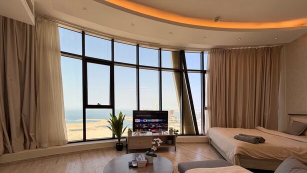 A hotel room with a large window, a bed, a sofa, a coffee table, and a TV. - Lovely Sea View Studio in Downtown F285O (Seef)