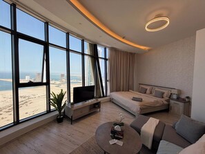 Habitació d'hotel moderna amb una finestra gran, un llit, un sofà, una televisió i una taula petita.