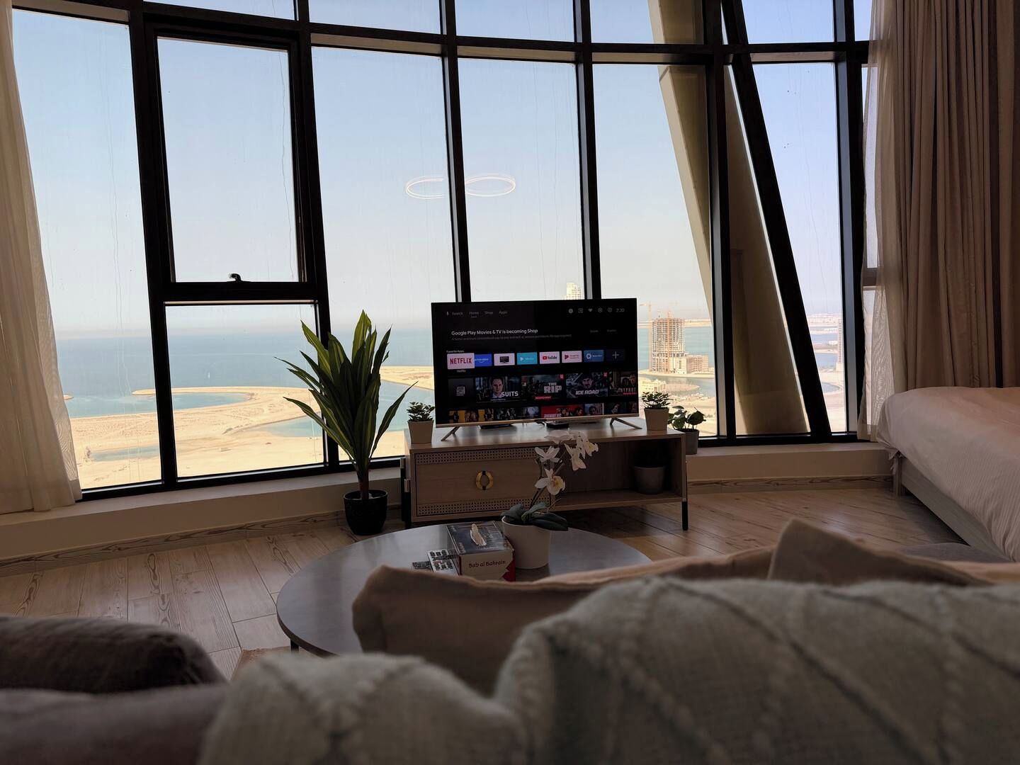 A modern living room with a large window, a flat-screen TV, a coffee table, and a sofa.