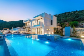 Uma casa moderna de dois andares, piscina, área de estar externa e vista para uma colina.