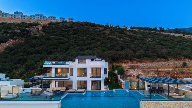 A modern two-story house with a swimming pool, outdoor seating, and a view of a hillside. - Vrbo Property (Kalkan)