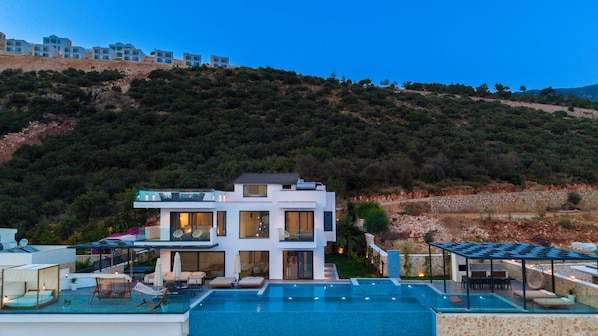 Uma casa moderna de dois andares com piscina, área de estar externa e vista para uma colina.