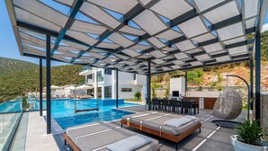 A rooftop pool area with two sunbeds, a dining table, and a hanging chair. - Vrbo Property (Kalkan)