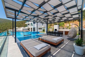 Área de piscina no terraço com duas espreguiçadeiras, uma mesa de jantar e uma cadeira suspensa.