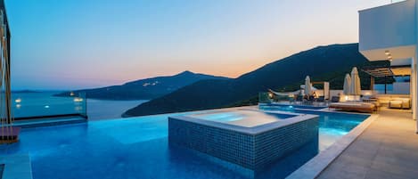 En modern infinitypool med utsikt över havet och bergen i skymningen.