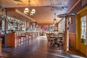A bar area with wooden floors, multiple seating arrangements, and a variety of bottles and glasses on shelves.