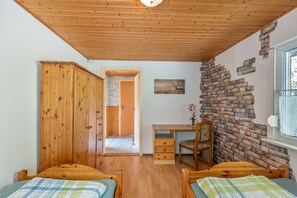 Ein Schlafzimmer mit zwei hölzernen Betten, einem Schreibtisch, einem Stuhl und einer Wandmalerei aus Ziegelsteinen.