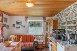 A cozy kitchen with wooden ceiling, a dining area with a sofa, and a brick wall with potted plants.