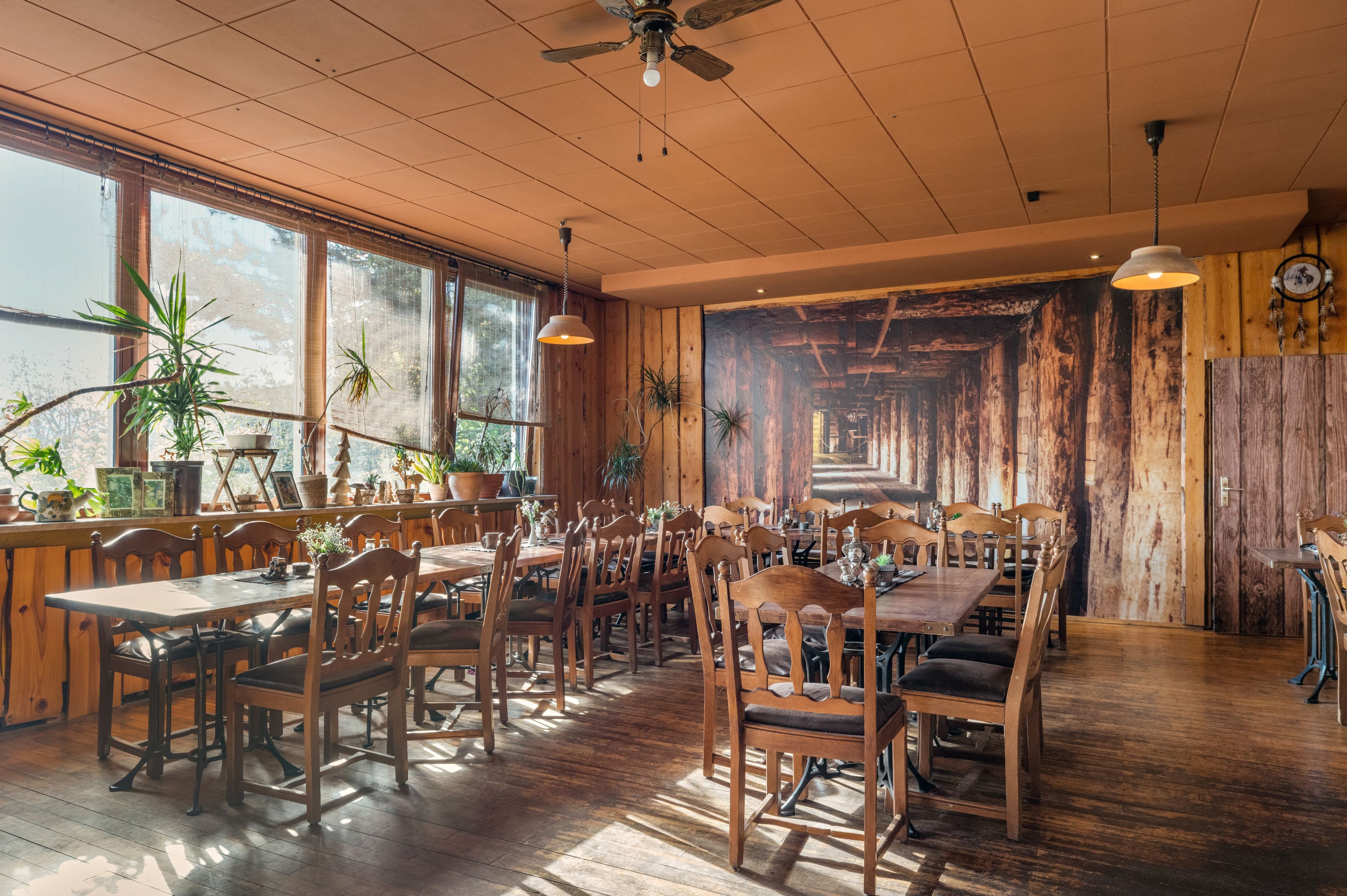 Ein Restaurant mit Holztischen und -stühlen, großen Fenstern und einem Deckenventilator.
